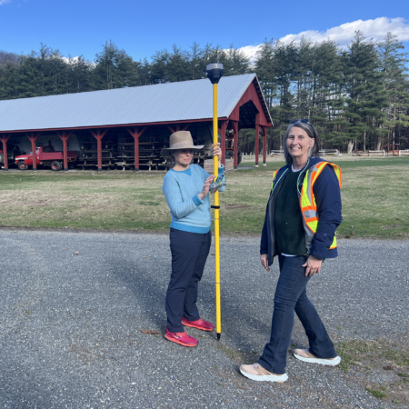 Two people with surveying equipment and a barn in the background